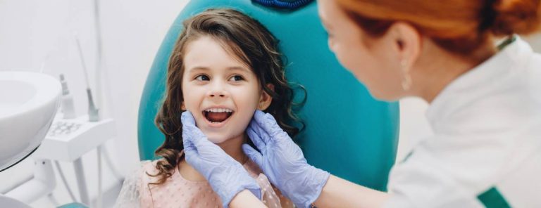 A young girl smiles brightly while seated in a dentist chair, showcasing a positive dental experience.