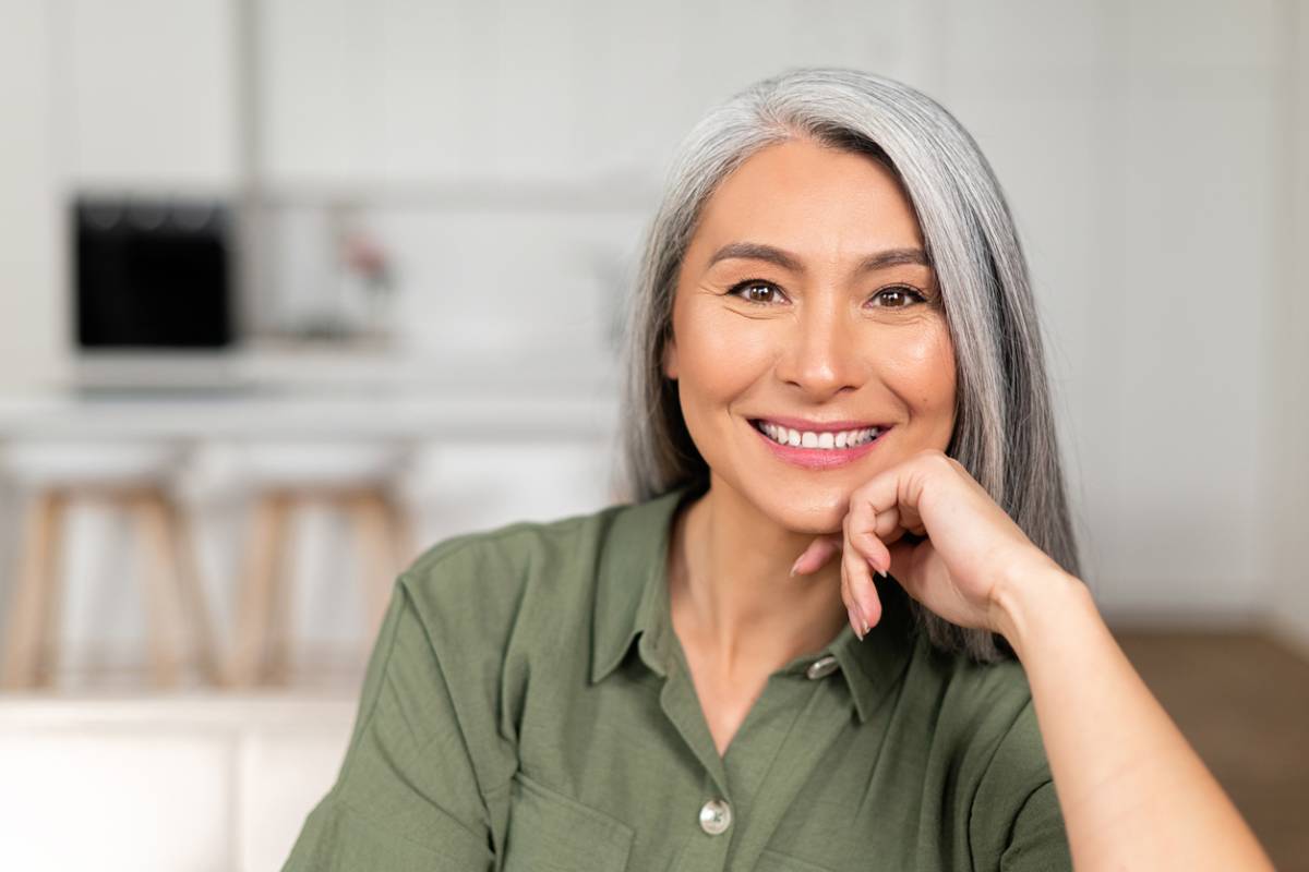 A smiling woman with gray hair, radiating warmth and positivity in a bright setting.