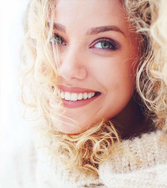 A cheerful woman with curly hair displays a bright smile, embodying happiness and warmth.