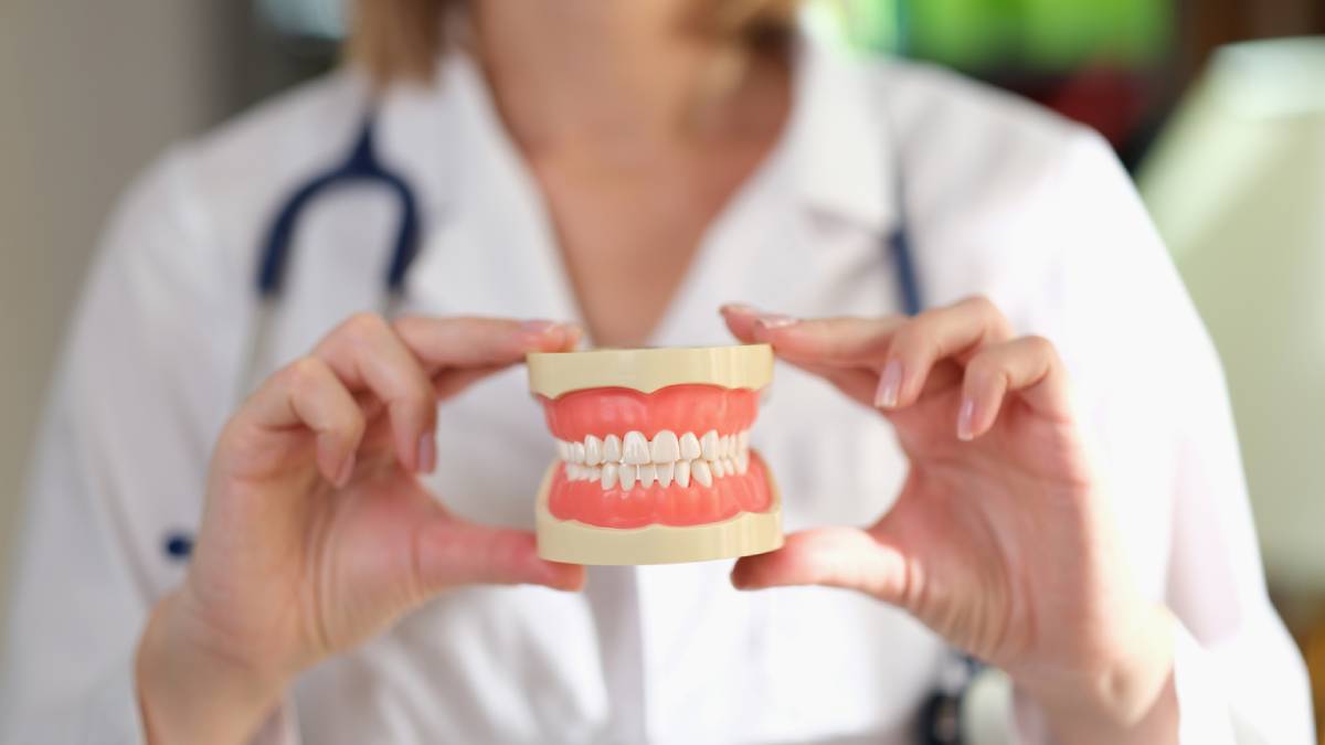 A woman holds a tooth model while wearing a stethoscope, symbolizing the connection between dental and overall health.