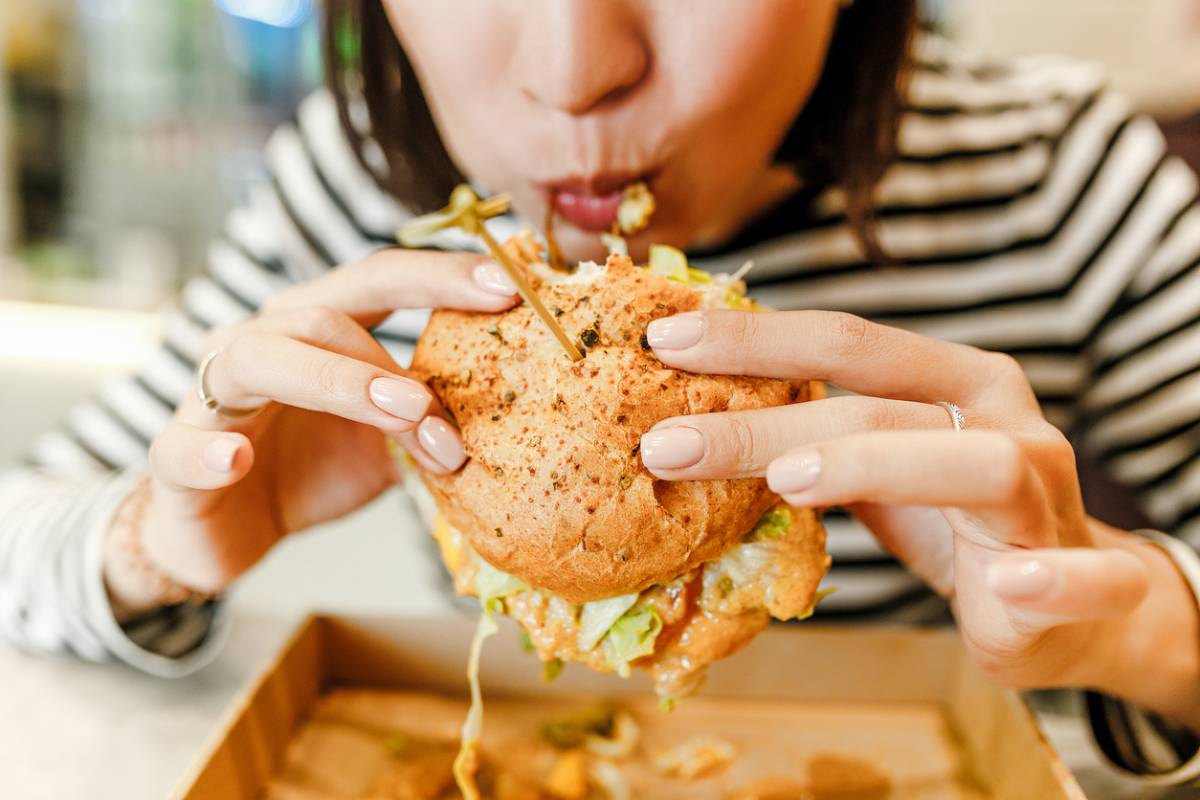 A woman enjoying a large hamburger, seated at a table with the meal presented in an open box before her.