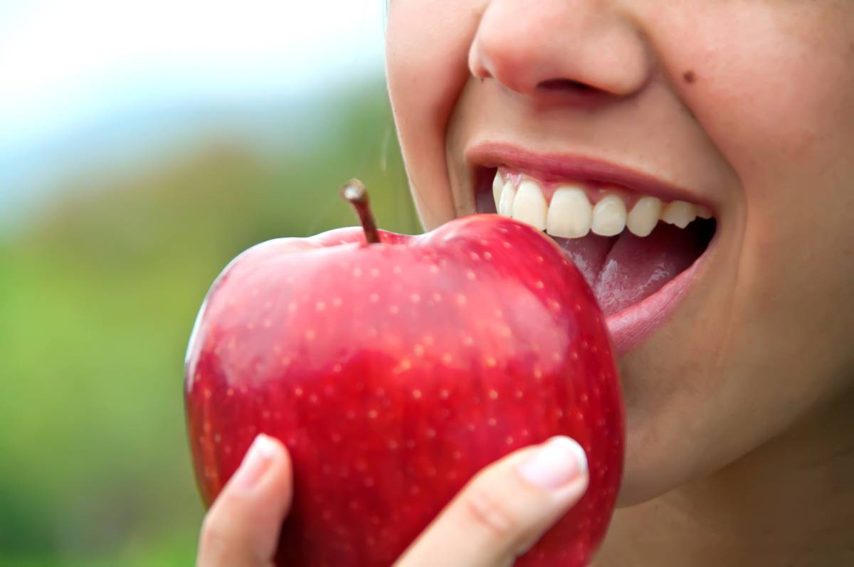 A woman smiles brightly while holding a fresh apple in her hand, radiating joy and health.