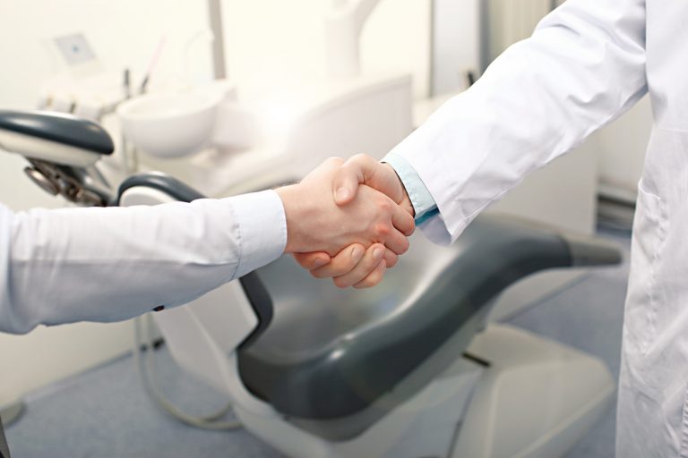 A man and woman shaking hands in a dental office, symbolizing a professional agreement or partnership.