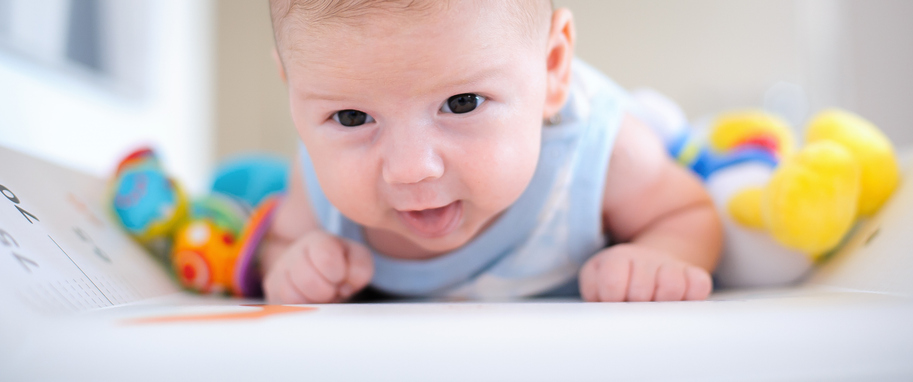 A baby lies on a white surface surrounded by colorful toys, creating a playful and cheerful atmosphere.