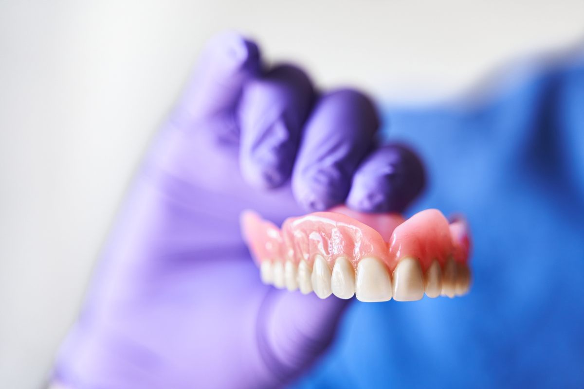 A person in gloves carefully holds a tooth alongside a denture, showcasing dental care and prosthetic solutions.