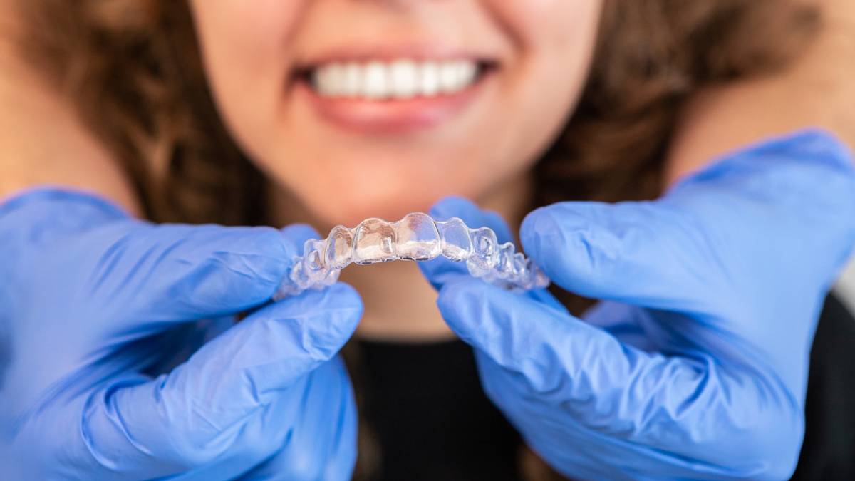 A woman wearing blue gloves is holding a clear aligner, showcasing dental care and orthodontic treatment.