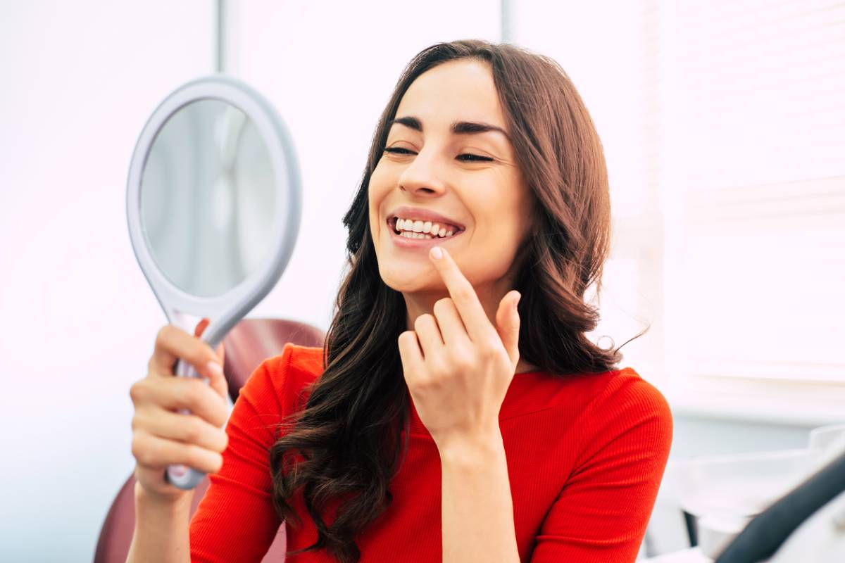 A woman gazes at her reflection in a mirror, examining her teeth with a thoughtful expression.