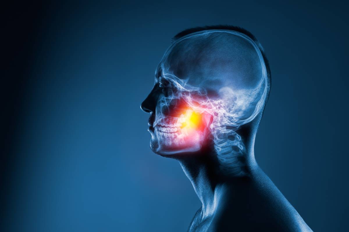 A man grimaces in discomfort, holding his jaw, indicating a painful toothache.