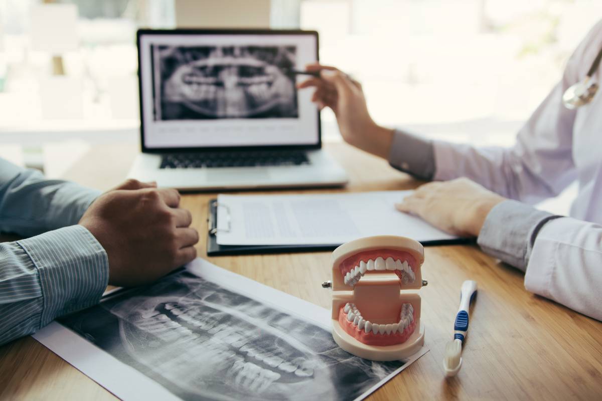 Dentist discussing dental problems with x-ray image on laptop screen to patient.