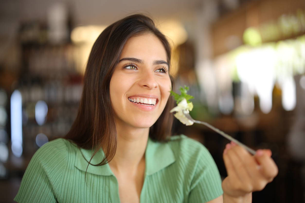 The image shows a woman eating salad for lunch to visualize which foods to avoid after teeth whitening